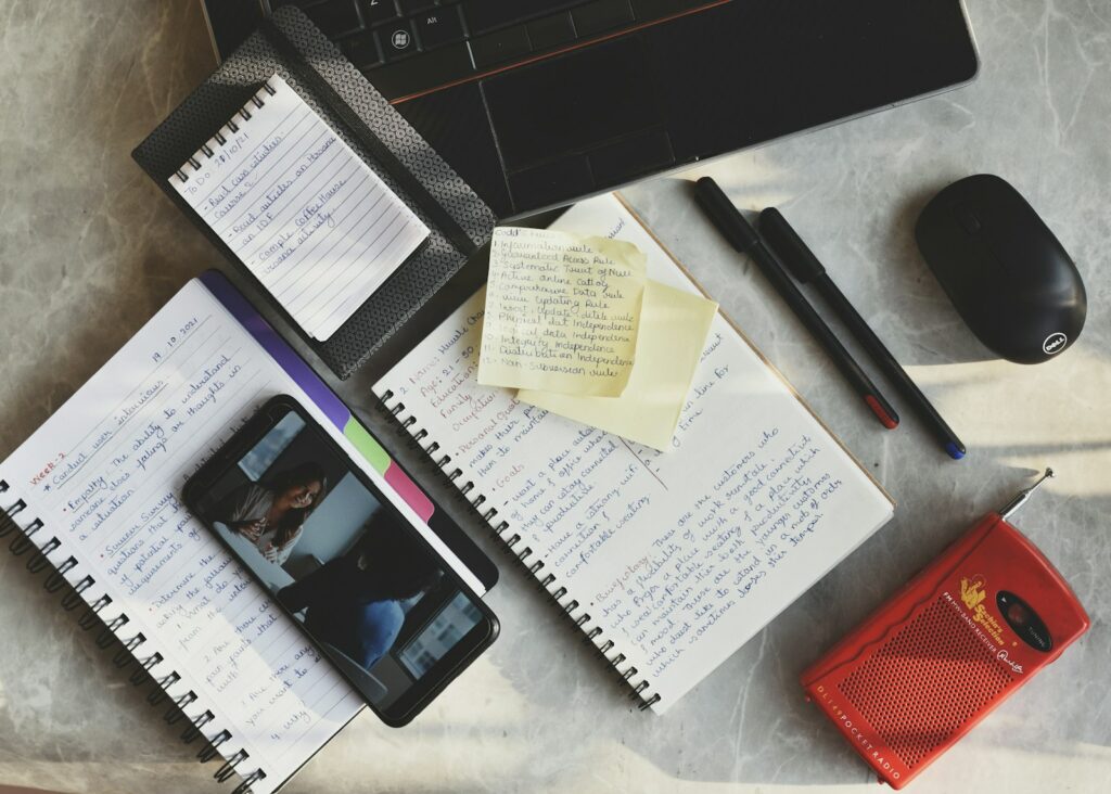 a desk with a laptop, notepad, pen, and cell phone