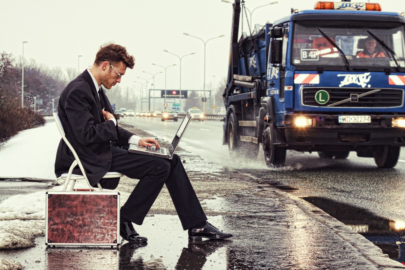 a man sitting on a suitcase on the side of the road